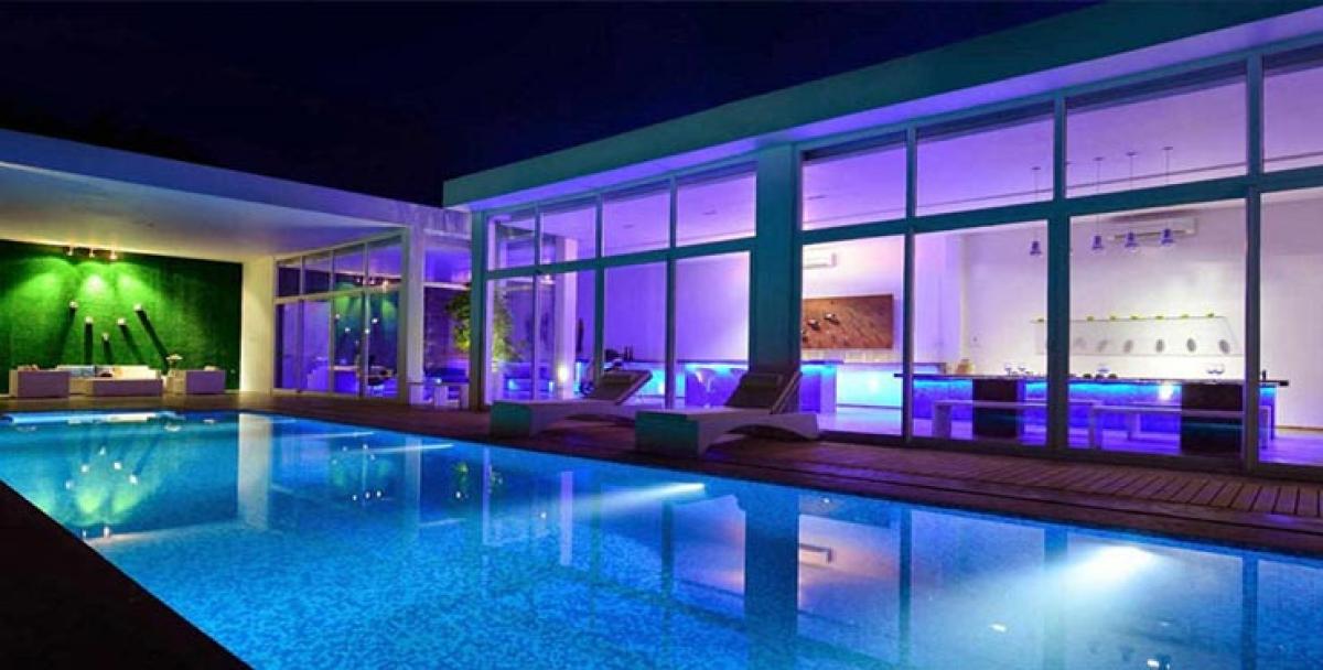 The lavish bathroom has a bathtub embedded into the flooring while it is surrounded by natural plants and skylight. The water closet and wash basin are set against a wall covered with slate tiles.