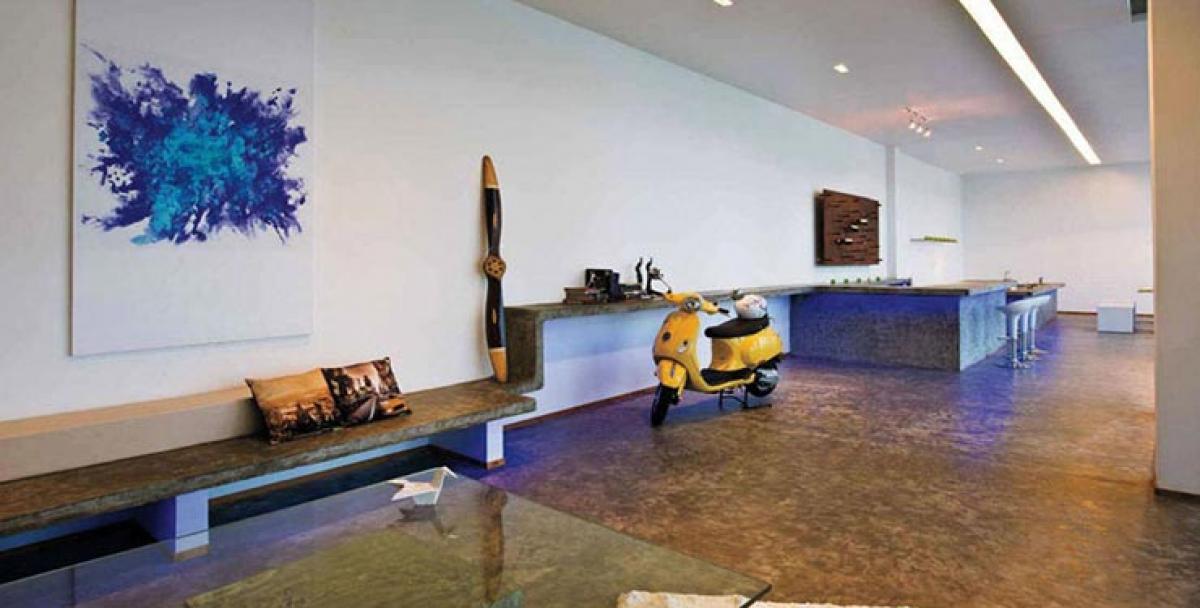 The living area has a seating made of cement with an epoxy finish which has been repeated on the flooring as well. The  stunning Piaggio Vespa bike in bright yellow brightens up the space.